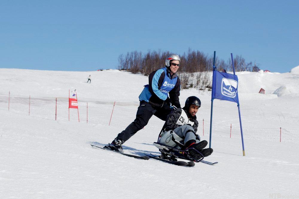 Gutt på sitteski med hjelper kjører alpint. Foto.