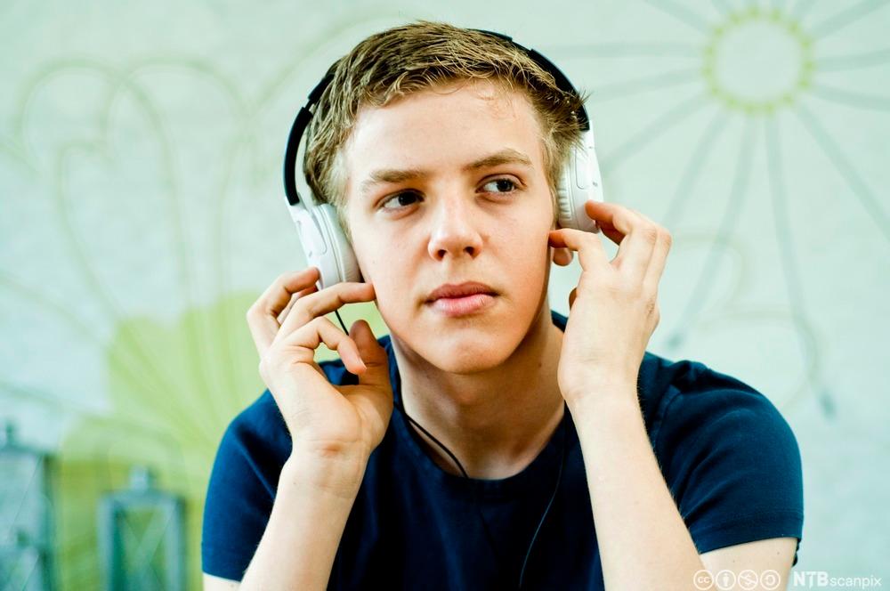 Gut lyttar til musikk ved hjelp av øyretelefonar. Foto.
