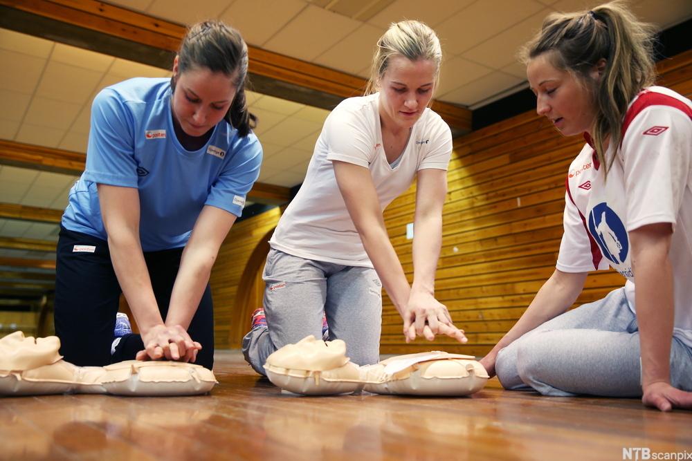 Tre personer øver på hjertekompresjoner på øvingsdokke. Foto.