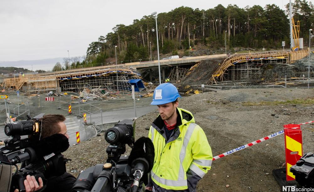 En mann med refleksvest og arbeidshjelm holder pressekonferanse på en byggeplass. Foto.