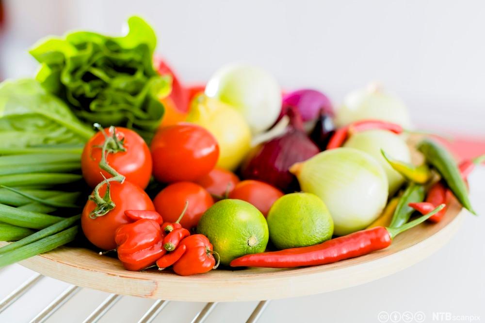 Fargerike grønsaker ligg på eit fat, mellom anna tomat, chili, lauk og salat. Foto.