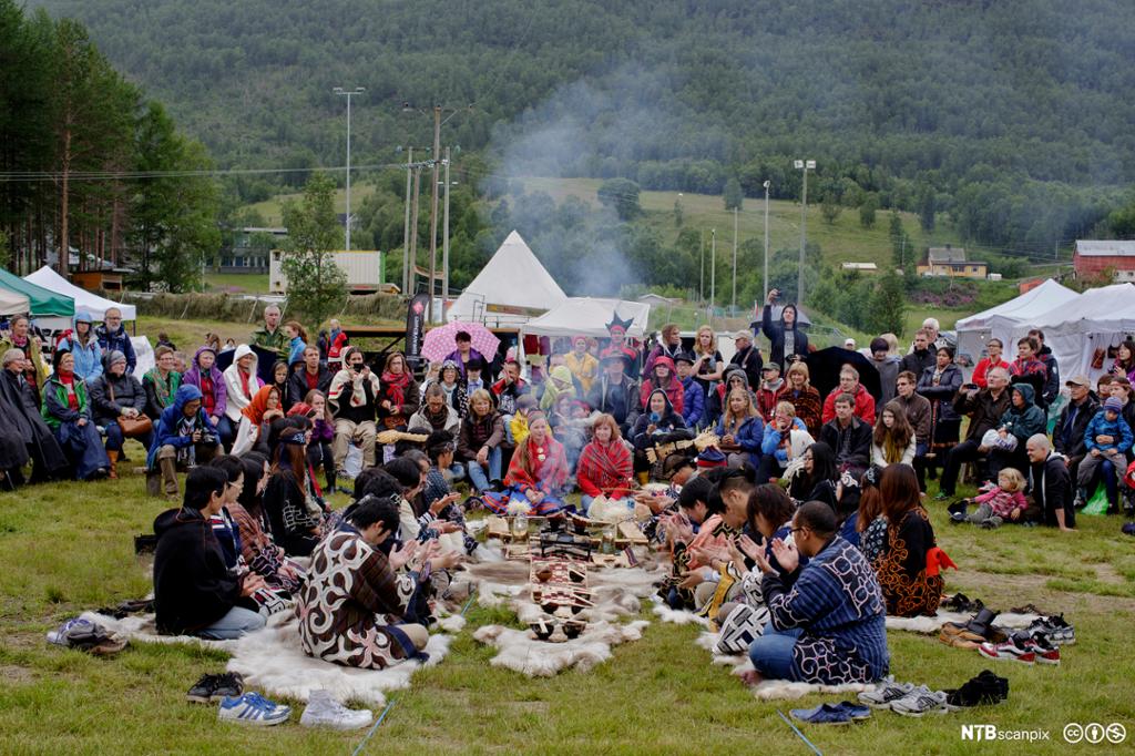 Ainu-folk og samer er kledd i nasjonaldrakter og sitter midt i en folkemengde på festivalområdet under Riddu Riddu-festivalen i 2013. Foto.