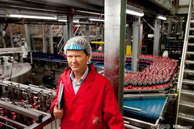 En mann står ved samlebåndet i produksjonshallen på en brusfabrikk. Foto