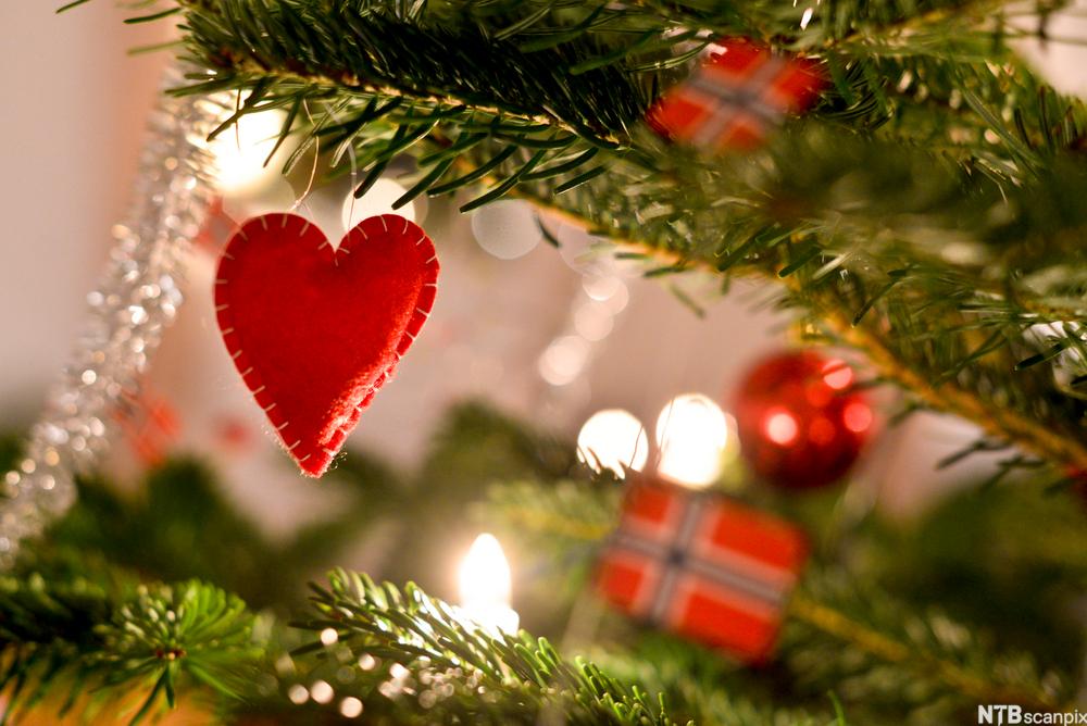 Julepynt som henger på juletreet. Vi ser et rødt hjerte i forgrunnen og norske flagg og julekuler i bakgrunnen.