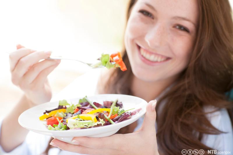 Ung kvinne spiser salat. Foto.