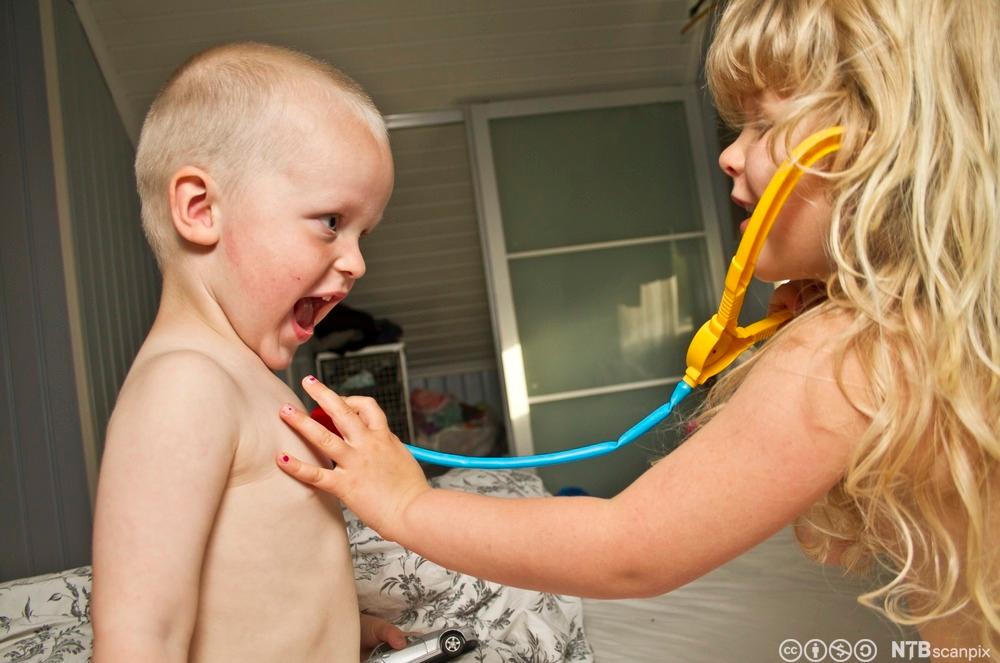 To små barn leker doktor, jenta holder et lekestetoskop mot brystet til gutten. Foto.
