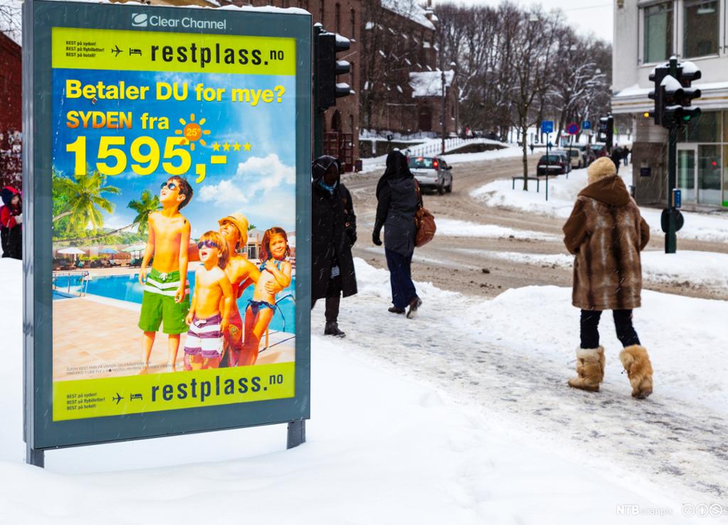 Reklameplakat for sydenreiser på snørikt fortau. Foto.