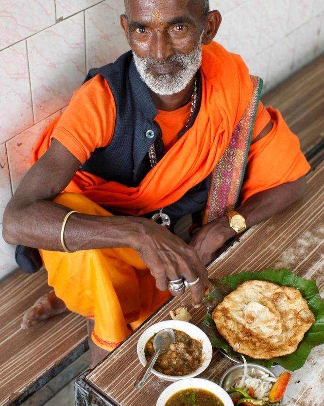 En sadhu spiser vegetarmat på en restaurant. Han har fargerike klær, gullklokke og sølvringer. Foto.