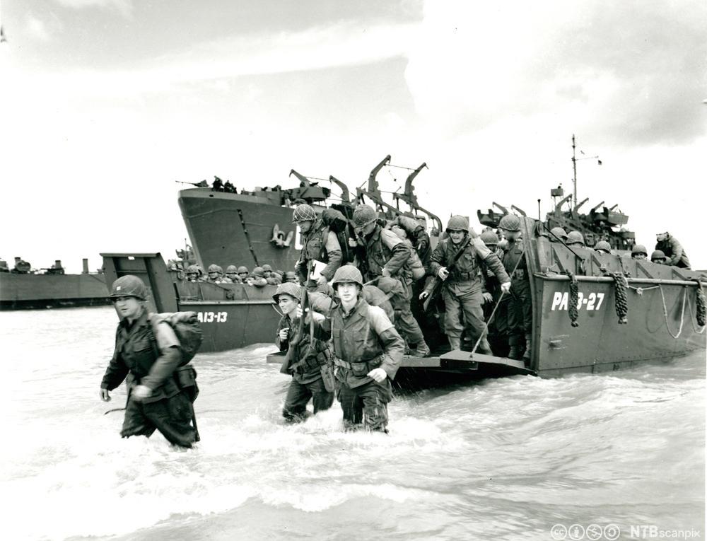 Soldater vasser i land fra militære båter. Svart-hvitt foto.
