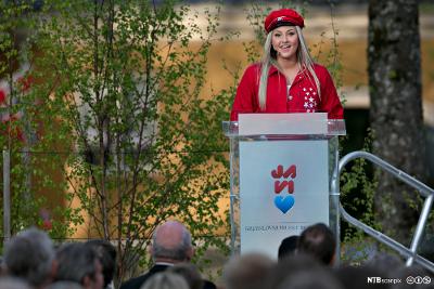 En russ i rød russedress holder 17. mai-tale foran en folkemengde på Eidsvoll. Foto.
