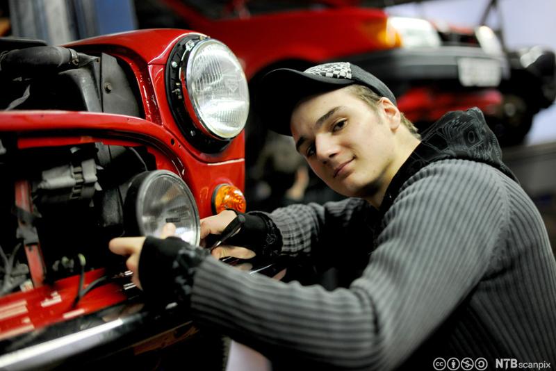 En gutt reparerer lykten på en bil. Foto.