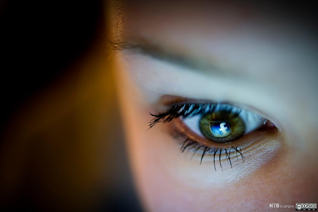 En jente ser på en skjerm, og Facebook-logoen speiles i øyet hennes. Foto.
