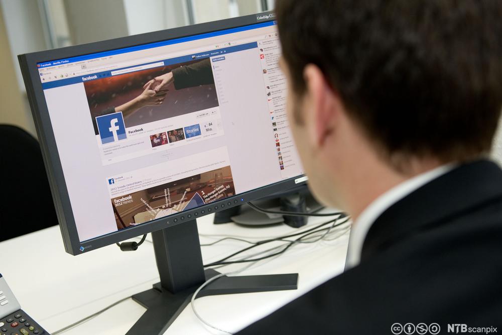 En mann sitter på Facebook på jobb. Foto. 