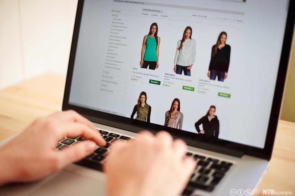 Handling på internett. Nærbilde av hendene til person som er inne på en nettside der man kan kjøpe klær. Foto.