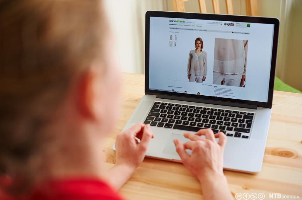 En person foran en laptop med nettside som viser klær. Foto. 
