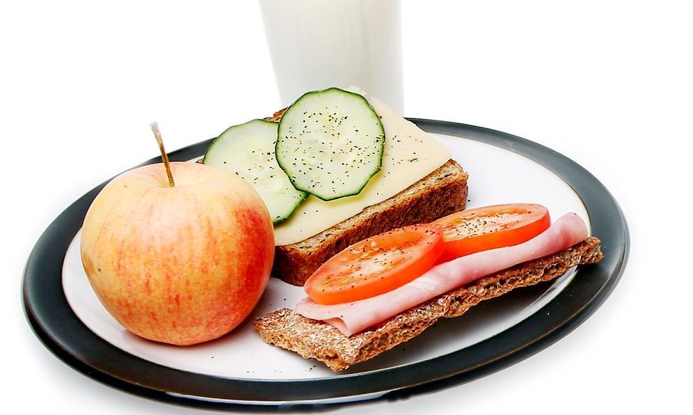 Foto av en tallerken med frokost med påsmurt brød og knekkebrød, frukt og grønt og melk.