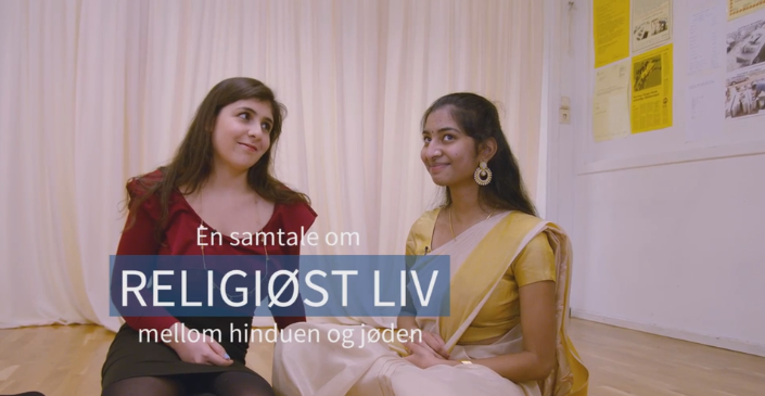 To unge kvinner sitter på gulvet. Innbrent tekst: "En samtale om religiøst liv mellom hinduen og jøden". Skjermbilde.