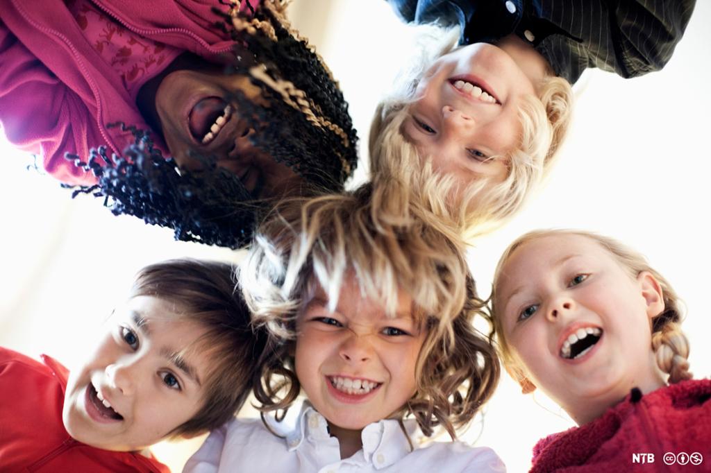  Fem barn stikker hodene sammen og smiler ned mot kamera. Foto.