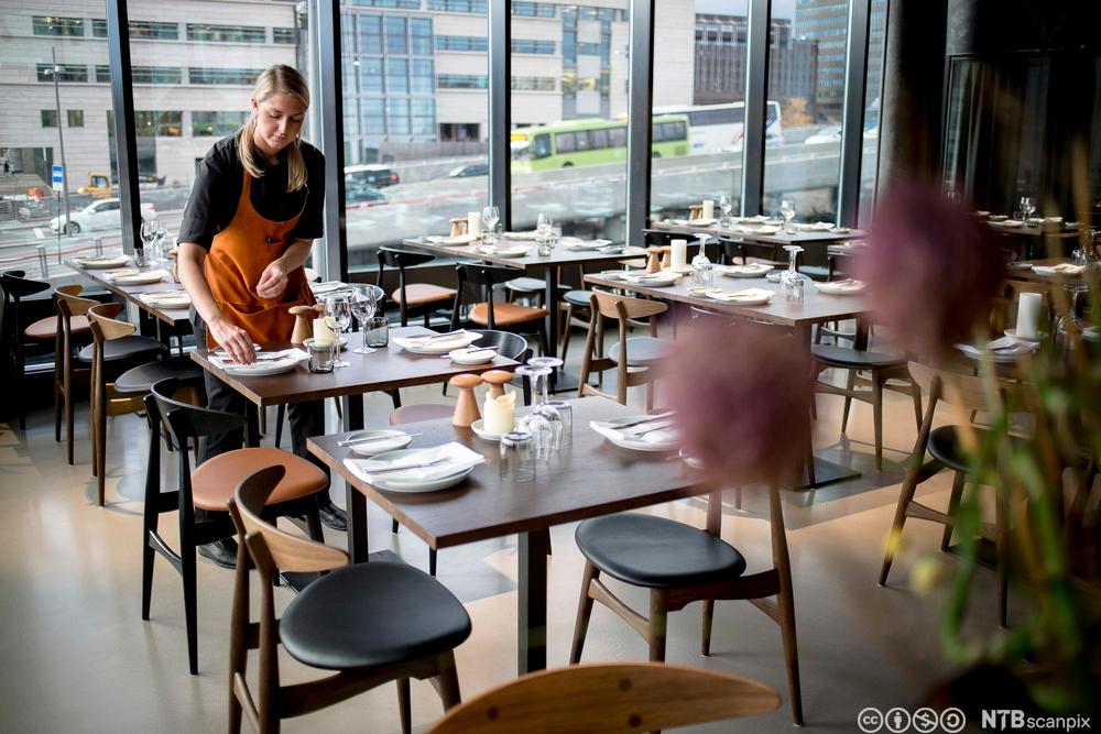En servitør dekker opp bord i en restaurant. Foto.