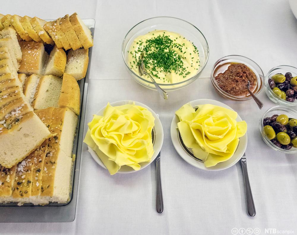 Focacciabrød på eit fat og smør, aioli, tapenade og oliven i skåler. Foto.