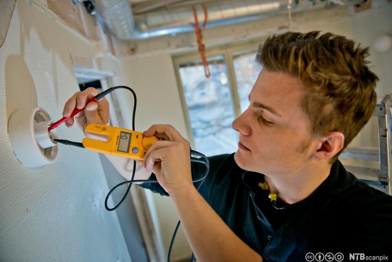 Elektriker måler elektrisitet i en vegglampe. Foto.