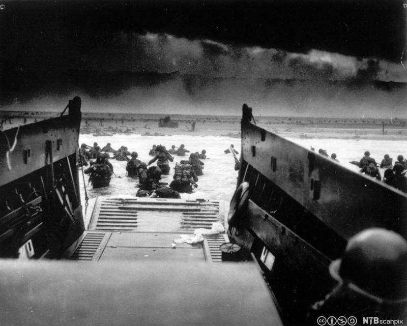 Soldater går i vannet fra landgangsfartøyene og mot stranda. Svart-hvitt-foto. 