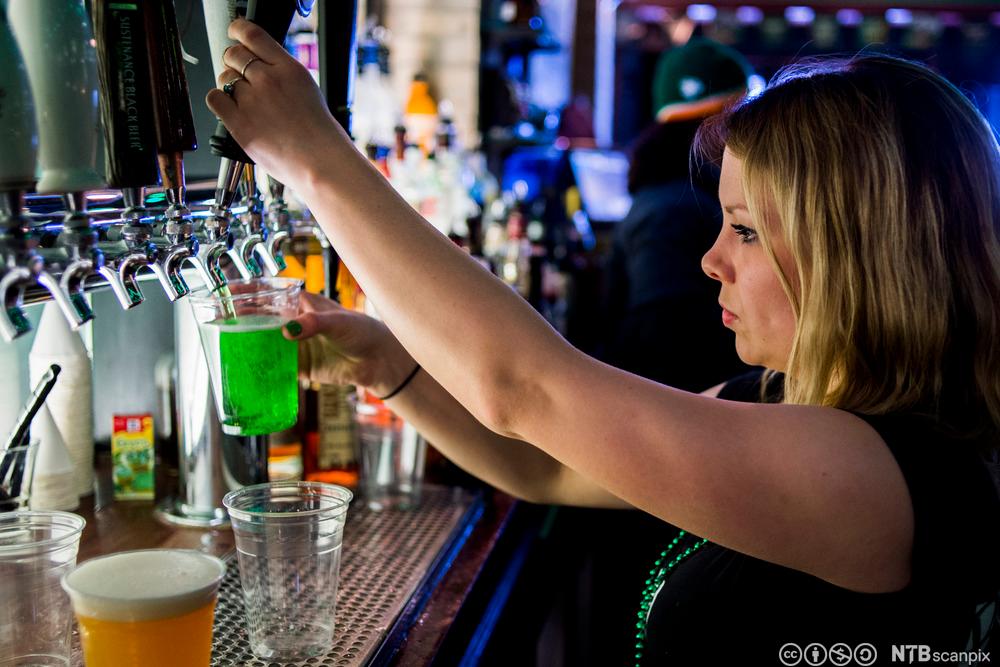 Bartender tapper grønn væske fra kran i tappetårn. Foto.