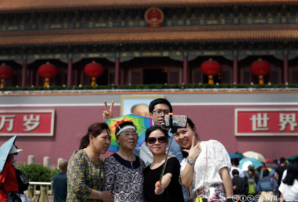 En kinesisk familie tar gruppeselfie utenfor på Tiananmen-plassen, foran Den forbudte by. Foto.