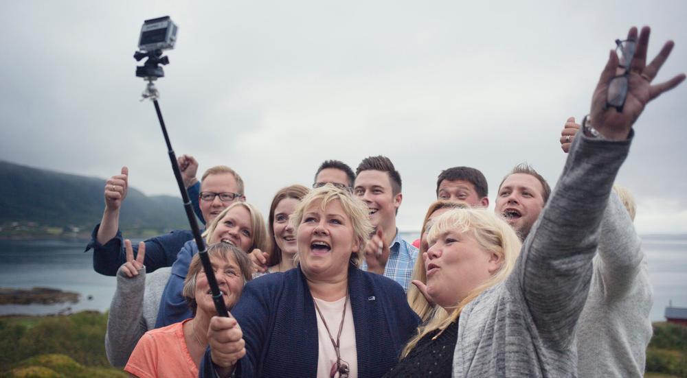 Erna Solberg holder i en selfiestang og tar selfie sammen med ei gruppe personer. Foto.