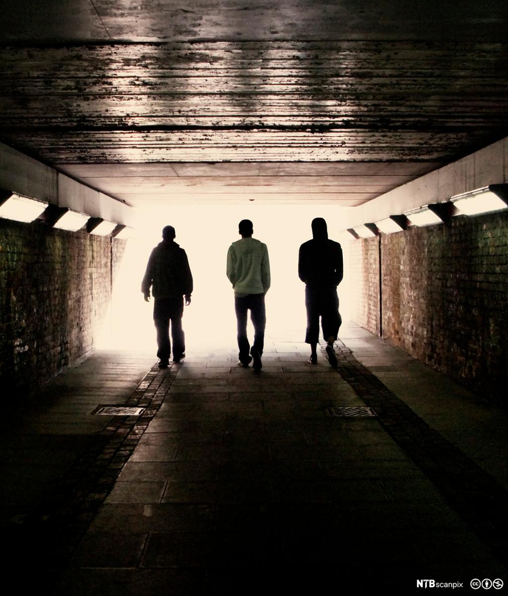Tre menn går sammen gjennom en undergang. Foto.