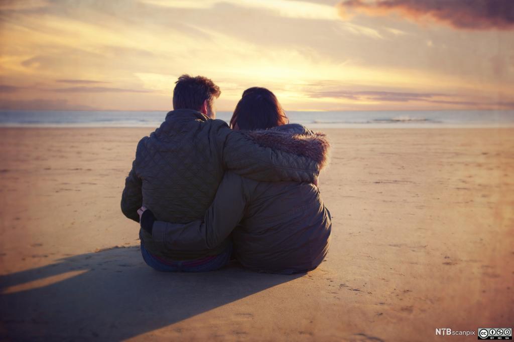 Kjærestepar sitter på stranden og ser på solnedgangen. Foto.