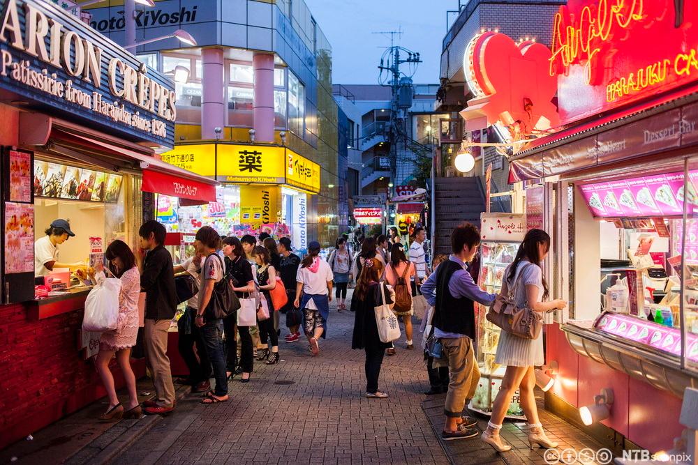 Menneskemengd i ei gate i Tokyo med ulike typar restaurantar og gatemat. Foto.