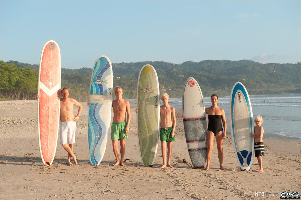 Familie med surfebrett på strand. Foto.