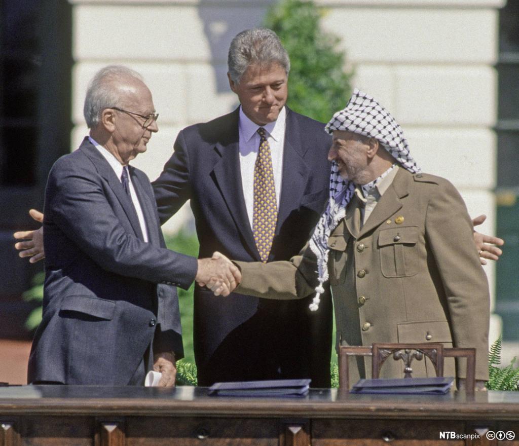 Yitzhak Rabin og Yasir Arafat tek kvarandre i handa medan president Bill Clinton står i midten og ser på. Foto.