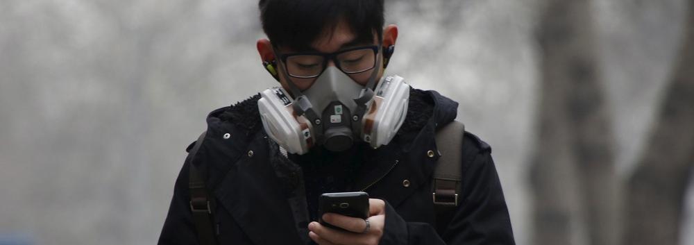 Mann har på seg kraftig maske for å beskytte seg mot forurensing. Han ser ned på mobilen sin. Foto.