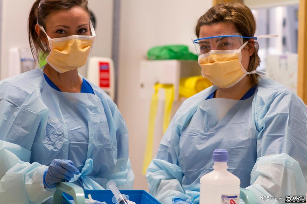  To kvinnelege helsefagarbeidarar ikledde blått smittevernutstyr. Foto.