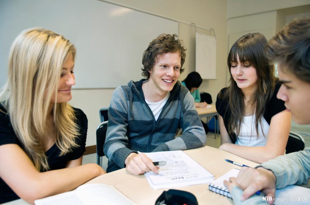 Elever sitter rundt pult i klasserom. Foto.