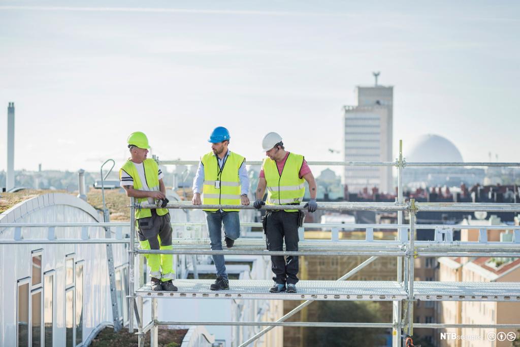 Tre arbeidere på stillas med hjelm. Foto.