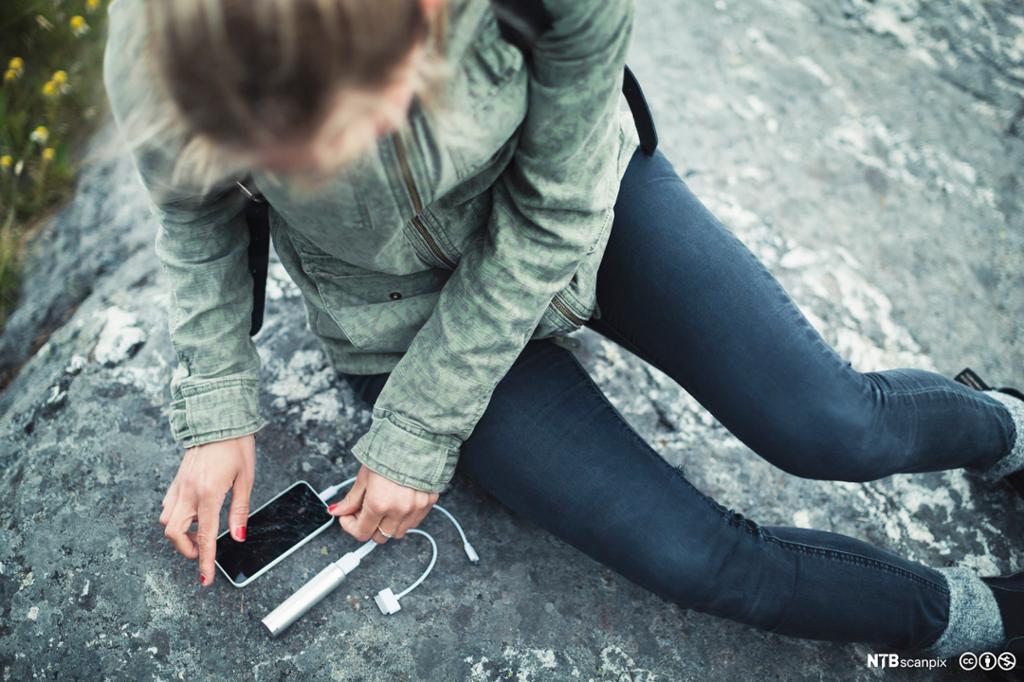 Kvinne kobler bærbar lader til mobiltelefon. Foto.