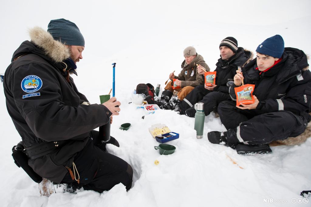 Turister spiser mat i snøen på Svalbard. Foto.