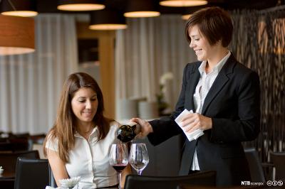 En kvinnelig servitør serverer vin til en gjest. Foto.