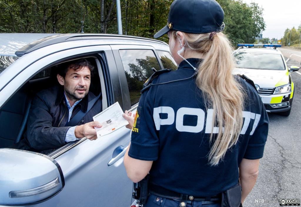 En kvinnelig politikonstabel sjekker vognkort og førerkort. Foto.