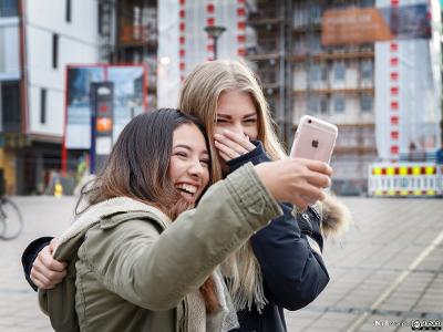 To jenter ler og tar selfie med en mobiltelefon. Foto.