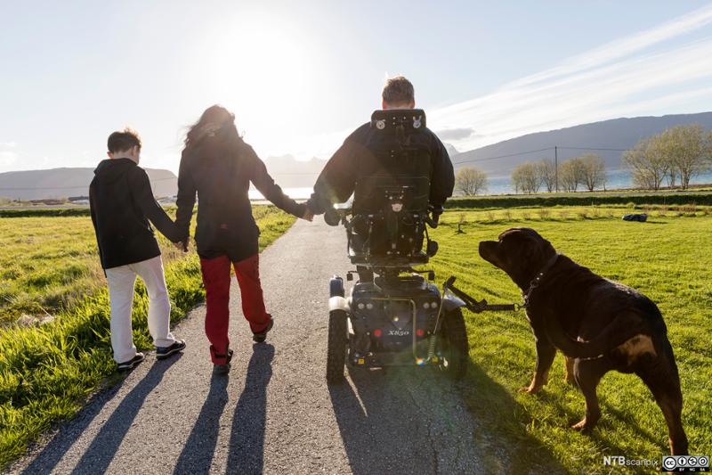 Mann i rullestol på tur med familien og hund. Foto.