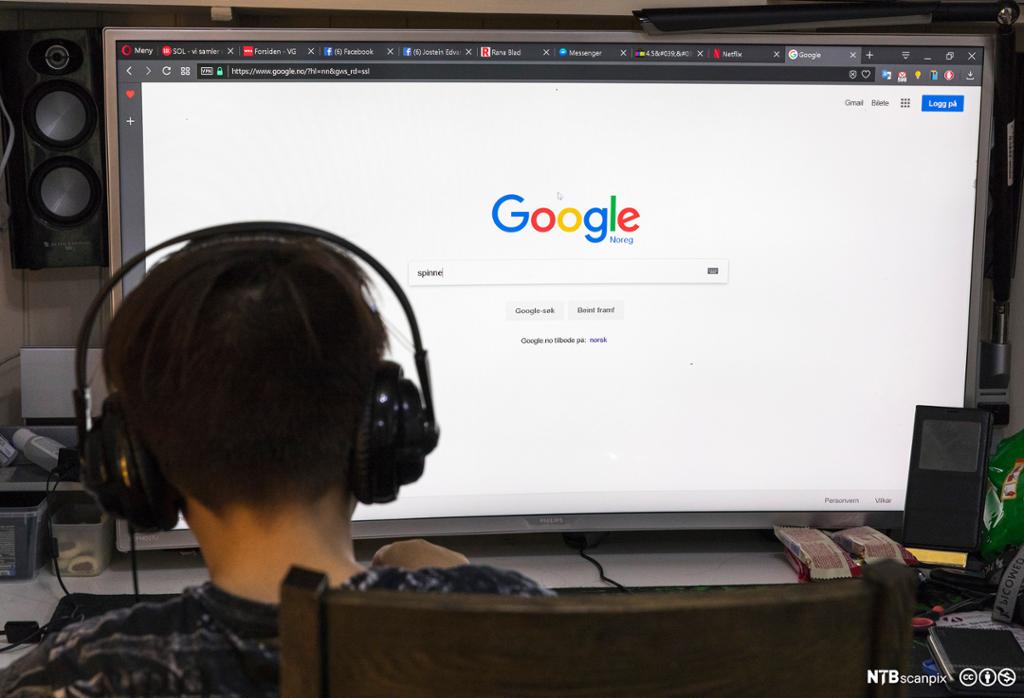 Ein gut med høyretelefonar sit framfor ein enorm pc-skjerm. På skjermen ser vi framsida til søkjemotoren Google. Foto.