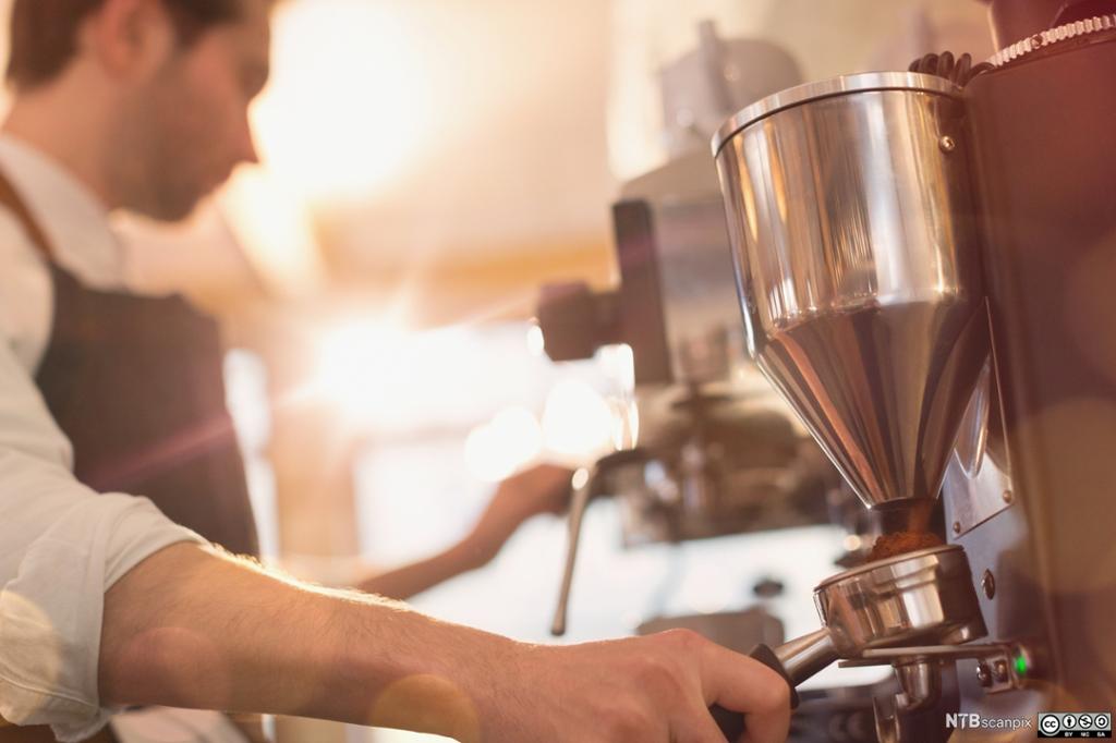 En mann kverner kaffe i en espressomaskin. Foto.