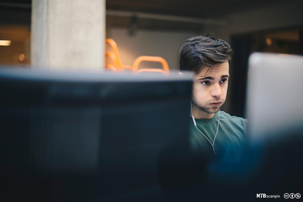 Ung mann sitter konsentrert ved stasjonær PC. Foto.