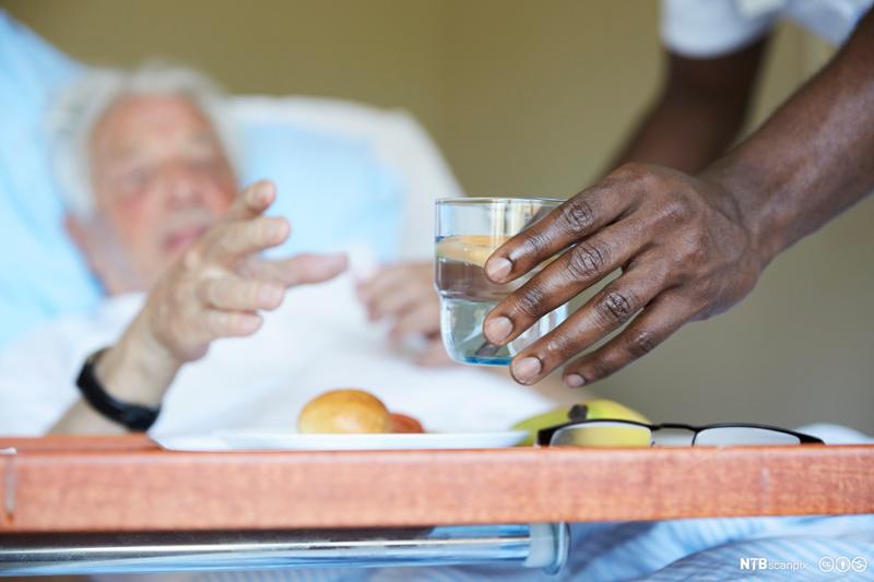 Pleier serverer vann til sengeliggende pasient. Foto.