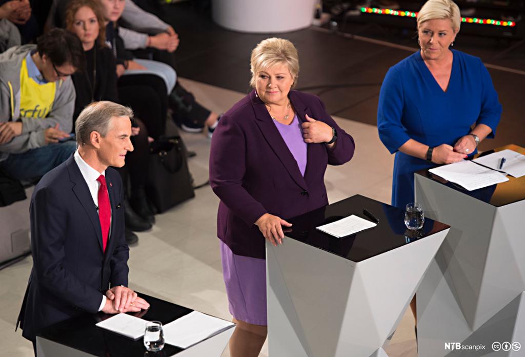 Jonas Gahr Støre frå Arbeidarpartiet, Erna Solberg frå Høgre og Siv Jensen frå Framstegspartiet står bak kvar sin talarstol og debatterer med tilhøyrarar i bakgrunnen. Foto.