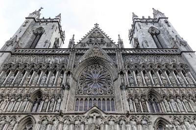 Fronten av katedral i gotisk stil med to tårn, helgenstatuer og rundt glassmaleri i sentrum. Foto.